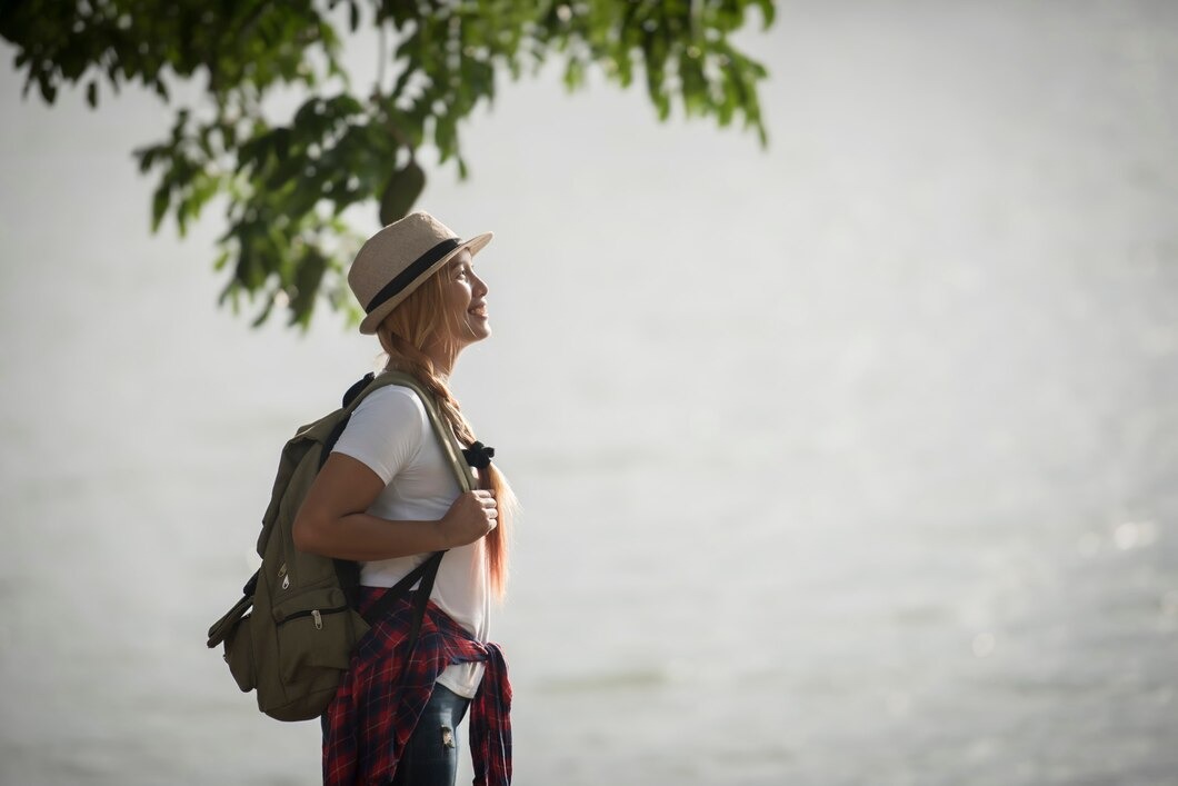 A woman with a backpack stands near the water, enjoying the view of the calm lake and surrounding nature